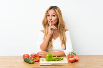 Young blonde woman with vegetables in a table doing silence gesture