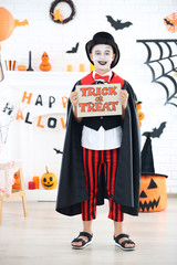 Young boy in halloween costume holding paper with text Trick or Treat