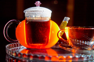Teapot and cup with light behind them and black background. Hot drink concept