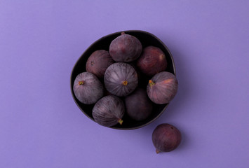 Obraz premium Fresh ripe figs in a bowl close up on a purple background.