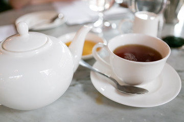 Earl grey tea in white teacup on saucer with teapot, cafe table, close up
