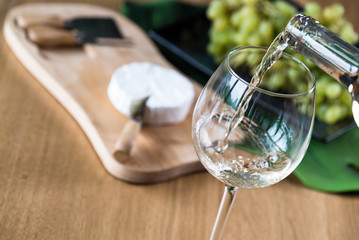 Pouring white wine into the glass against wooden background