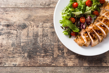 Grilled chicken breast with vegetables on a plate on wooden table. Top view. Copy space