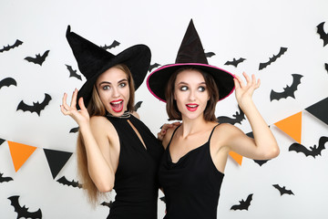 Two young women in black halloween costumes with paper bats and flags on white background