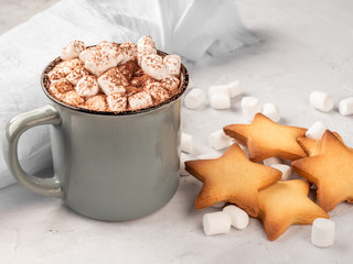 Hot chocolate in a gray mug with cookies on a concrete surface.