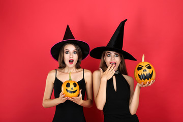 Two young women in black costumes with halloween pumpkin on red background