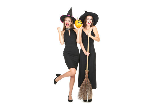 Two young women in halloween costumes with broom and pumpkin on white background