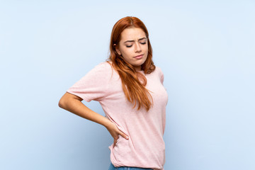 Teenager redhead girl over isolated blue background suffering from backache for having made an effort