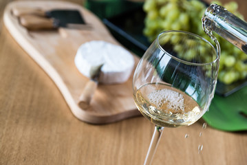 Pouring white wine into the glass against wooden background
