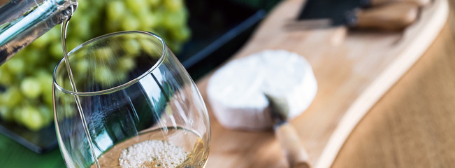 Pouring white wine into the glass against wooden background