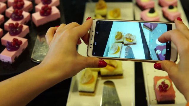 A woman photographs on a smartphone pieces of cake and desserts. Social network blogger concept photo. Healthy and tasty food.