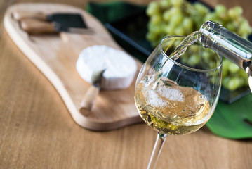Pouring white wine into the glass against wooden background