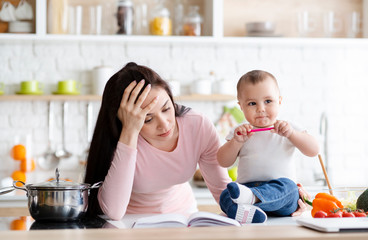 Tired mother holding head, trying to work at home but baby disturbing her