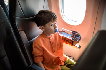 Charming kid traveling by an airplane. Little boy drinking water during the flight. Air travel with little kids