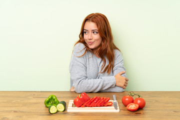 Teenager redhead girl with vegetables in a table thinking an idea