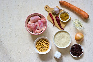 Ingredients for cooking pilaf on a light concrete background: chicken, rice, raisins, carrots, vegetable oil, spices, boiled chickpeas, garlic, hot pepper, salt. Top view. Recipe card.