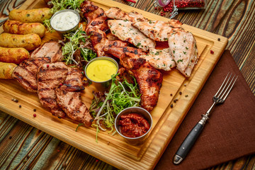 Assorted delicious grilled meat and vegetables with fresh salad and bbq sauce on cutting board on wooden background. Big set of Hot Meat Dishes