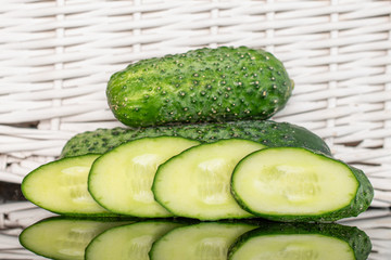 Group of two whole four slices of fresh pickling cucumber with braided rattan behind