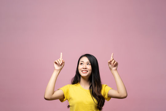 Portrait Of Smiling Asian Beautiful Young Woman Presenting With Two Hand Finger Point On Upper Side To Copy Space. The Girl Standing And Looking Up At In Studio. Advertisement & Presentation Concept.