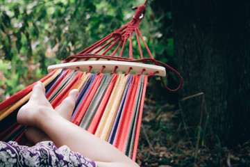 Close-up of the legs of a girl in a multi-colored striped hammock on a backdrop of green forest, selective focus