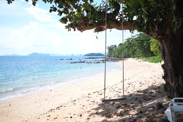 Beach with trees hanging by swings And there is a blue sky Surrounded by islands
