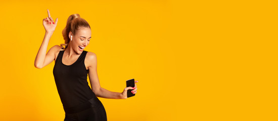 Happy Sporty Girl Holding Mobile Phone Dancing Over Yellow Background
