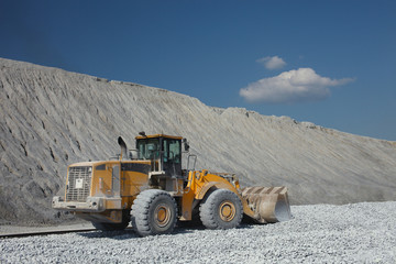 Wheel loader excavator against the backdrop of waste rock dumps and blue sky with clouds. Heavy equipment.