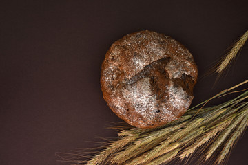 Loaf of bread and ears of wheat on a dark background, top view.