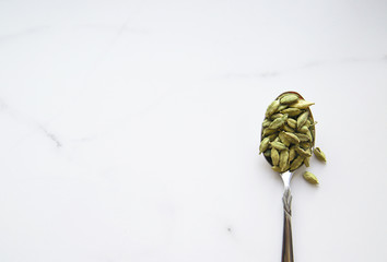 Cardamom seeds in spoon and copy space. Green and healthy spice concept. Seasoning for food and drinks. Top view and flat lay
