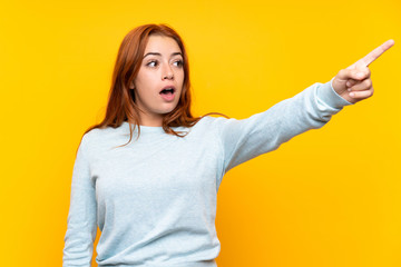 Teenager redhead girl over isolated yellow background pointing away