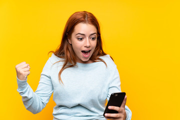 Naklejka premium Teenager redhead girl over isolated yellow background surprised and sending a message