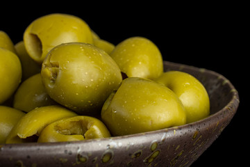Lot of whole pitted green olive closeup on grey ceramic plate isolated on black glass