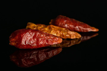 Group of three whole dry red chili pepper peperoncino in row isolated on black glass