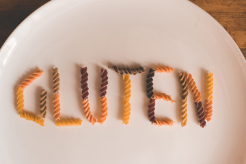 White plate with fusilli pasta in word gluten close up. Unhealthy eating. Top view. Selective focus.