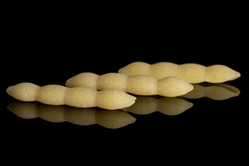 Group of three whole uncooked pasta cavatelli in row isolated on black glass