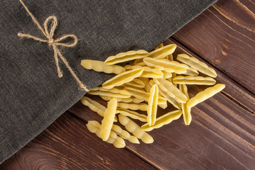 Lot of whole uncooked pasta cavatelli with grey textil napkin flatlay on brown wood