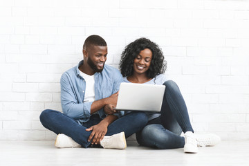 Happy couple sitting on floor, using laptop in new house