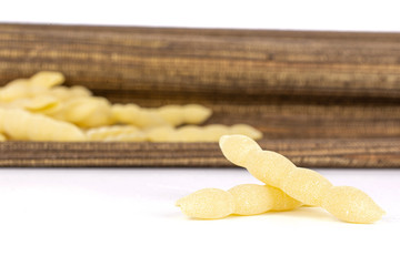 Lot of whole uncooked pasta cavatelli two in focus with brown textil cloth isolated on white background