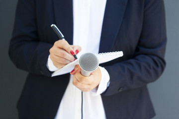 Female journalist at news conference or media event, writing notes, holding microphone