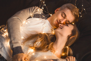 couple in love in a cozy room cuddles among the New Year's garland of lanterns