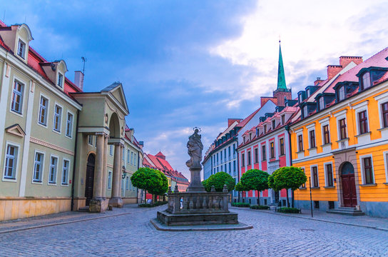 Cobblestone street road with colorful buildings and Statue of Madonna and Child monument with blue cloudy sky background in old historical city centre, evening view, Ostrow Tumski, Wroclaw, Poland