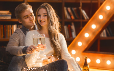 couple in love drinks champagne in a cozy room with a large lamp in the form of a letter and Christmas lights
