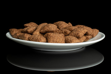 Lot of whole crispy brown cereal pillow on white ceramic plate isolated on black glass