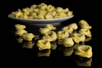 Lot of whole fresh yellow spinach filled tortelloni on white ceramic plate isolated on black glass