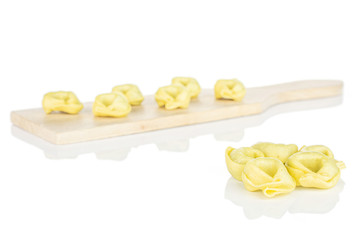 Lot of whole fresh yellow spinach filled tortelloni on small wooden cutting board isolated on white background