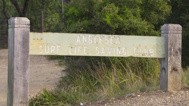 A daylight closeup shot of the signage of the Anglesea Surf Lifesaving Club carved in a wood board and fixed between two thick wooden posts.