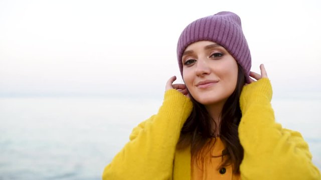 Young pretty woman in mangenta hat and yellow tarp turning around on the background of sea