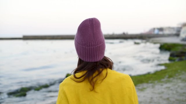 Young pretty woman in mangenta hat and yellow tarp turning around on the background of sea