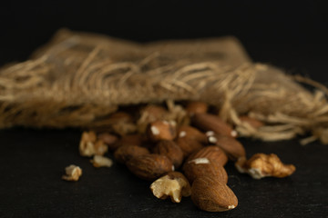 Lot of whole brown almond nut heap with jute fabric isolated on grey stone