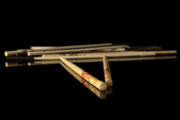 Lot of whole crossed asian brown chopsticks isolated on black glass